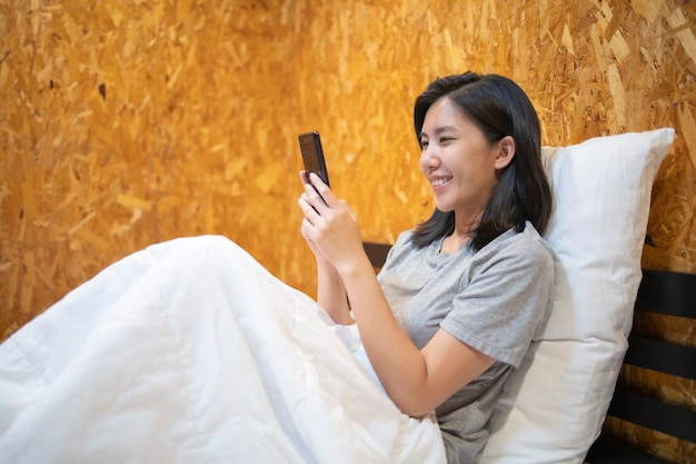 A girl sleeping on a white mattress and playing with a mobile phone