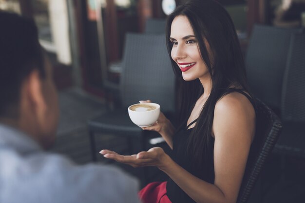 The girl smiles and holds a mug of cappuccino in her hand 