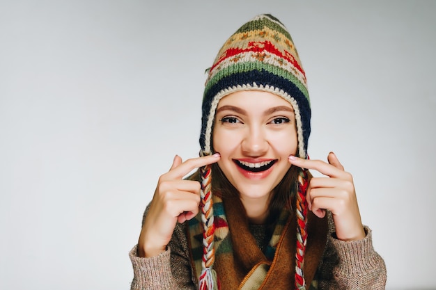 The girl smiles and shows on her cheeks, wearing a hat and a scarf with a scandinavian ornament