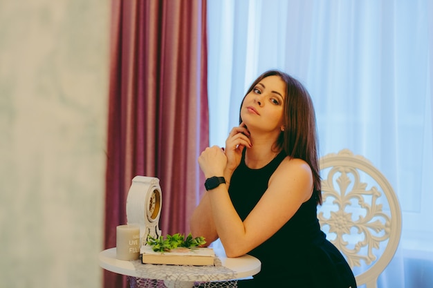 Photo girl smiles sitting on a chair, dressed in black, at a small round table