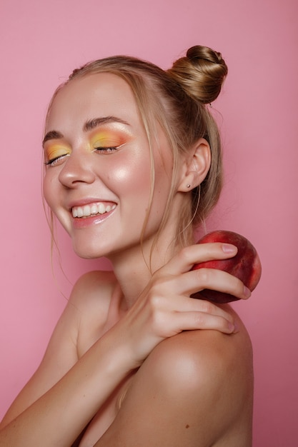 La ragazza sorride con trucco luminoso e pesca su una parete rosa. foto estiva brillante