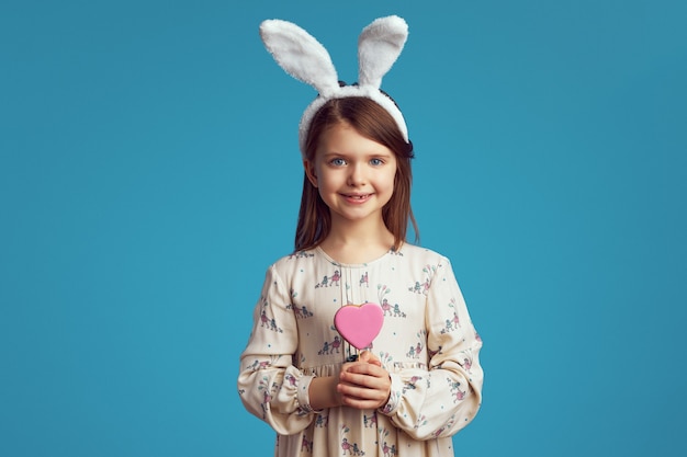 Girl smiling and holding a cookie in shape of heart over blue wall