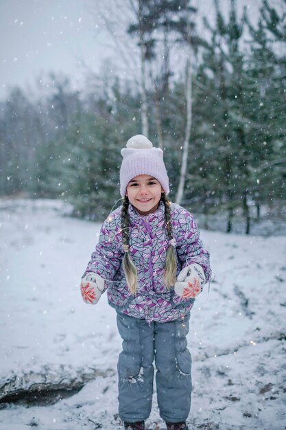 雪の日に森の中を歩いている間、笑顔と笑いの女の子が輝く花輪で遊ぶ