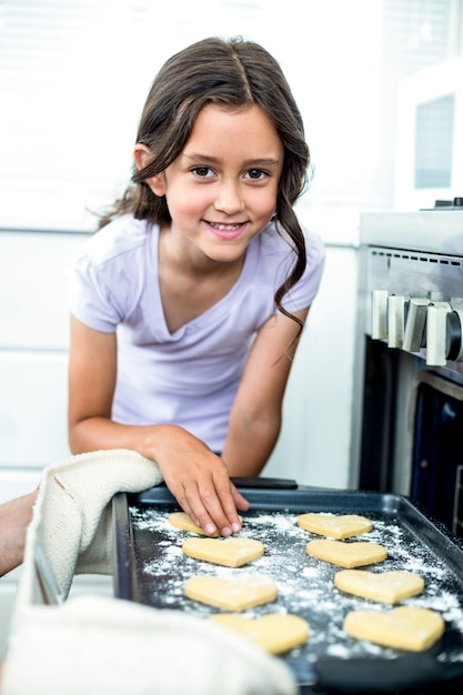 Ragazza che sorride mentre toccando i biscotti di forma del cuore in vassoio