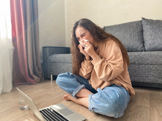 Girl sneezes into a handkerchief sitting on floor near the laptop