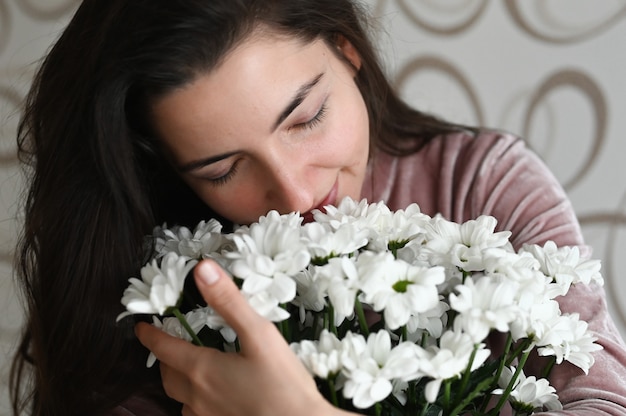 La ragazza annusa un mazzo di fiori bianchi. abbracci bruna annusa un bouquet di delicati fiori dalla sua amata. un bel regalo per la tua amata metà.