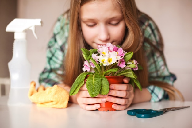 Una ragazza annusa un fiore e si prende cura delle piante nella sua casa, primo piano