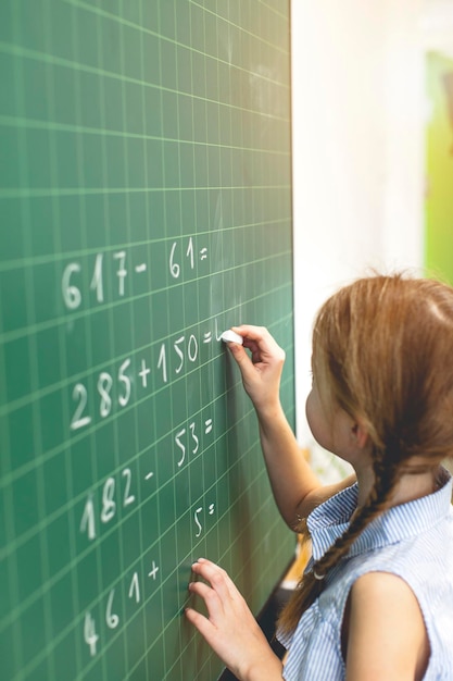 Girl solving mathematics equation on blackboard in classroom at school