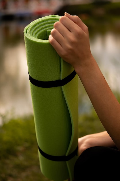 Una ragazza in uniforme sportiva tiene in mano un tappetino da yoga vestita con un top sportivo nero su un tappetino sportivo