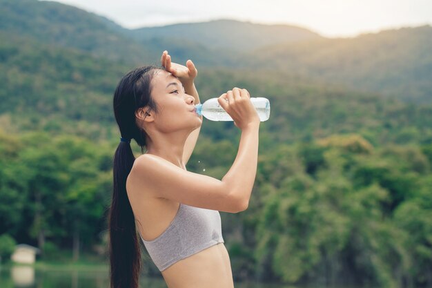 スポーツウェアの女の子は、トレーニング後に屋外の公園で再生プラスチックボトルから水を飲む