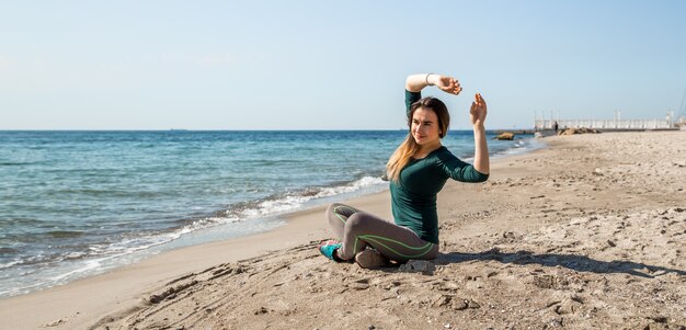 Girl in sportswear fitness by the sea listening