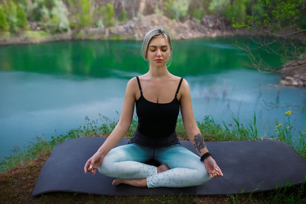 Girl in sportswear meditates near the lake