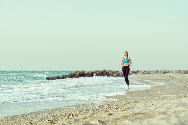 Girl in sportswear running along the surf line. 