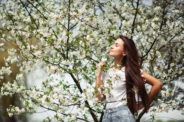 Foto ragazza che sta sotto di melo sbocciante in parco naturale.