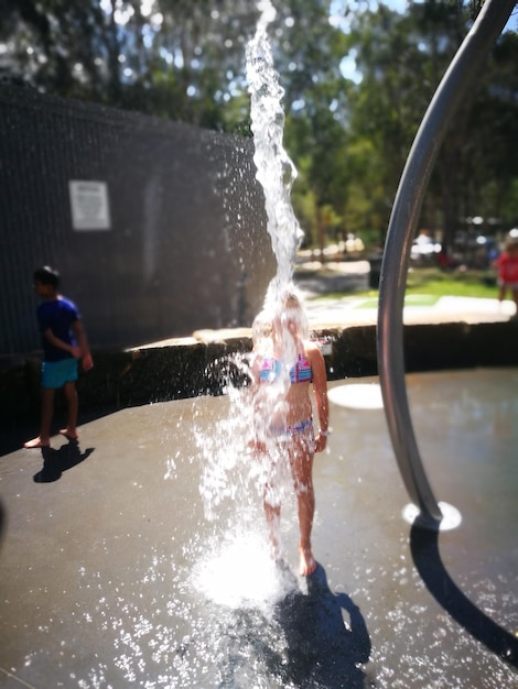 Foto ragazza in piedi sotto l'acqua che cade al parco