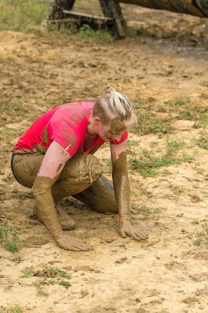 Девушка стоит на коленях, вытирая грязь с рук о землю после преодоления препятствия.