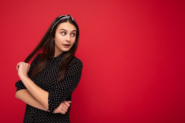 girl standing isolated over red wall wearing casual stylish black clothes looking to the side. copy space