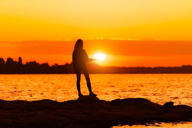 手元に太陽を保持している岩の上に立っている女の子自然と美しさの概念オレンジ色の日没日没時の女の子silhuette