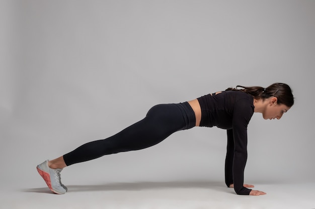 Photo girl standing in plank on straight arms on grey wall