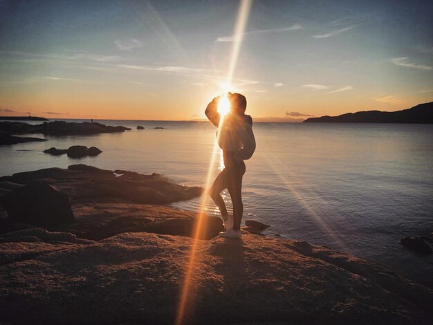 Photo girl standing on rock at beach against sky during sunset