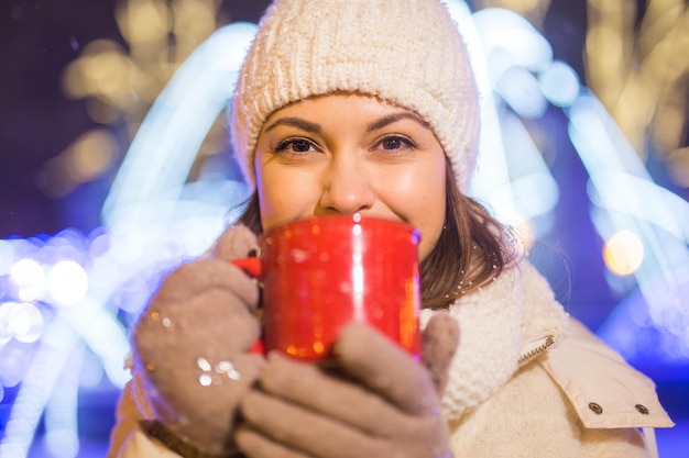 Девушка стоит на зимнем рождественском фоне города снег сугробы стоит теплая куртка шляпа держит