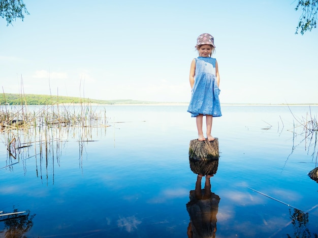 Girl standing on wooden post over lake against sky