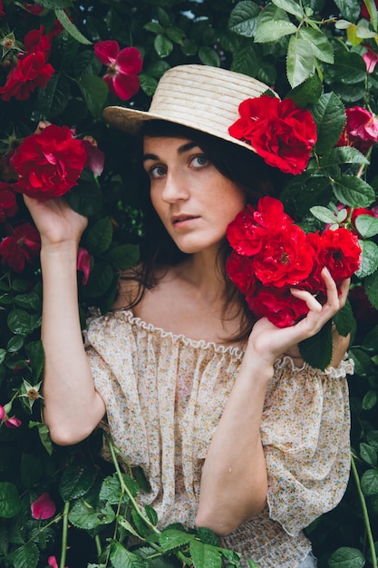 La ragazza sta contro un muro di cespugli con rose rosse