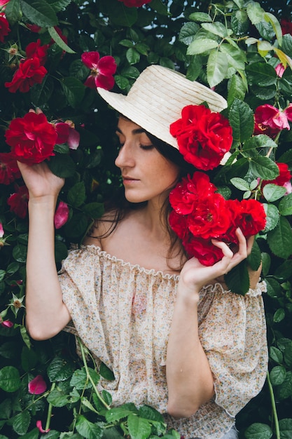 Girl stands against a wall of bushes with red roses