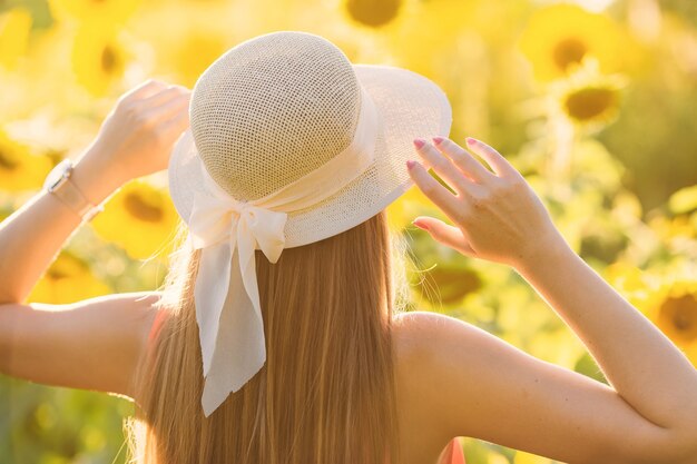 The girl stands back to the camera and holds her hands on the hat