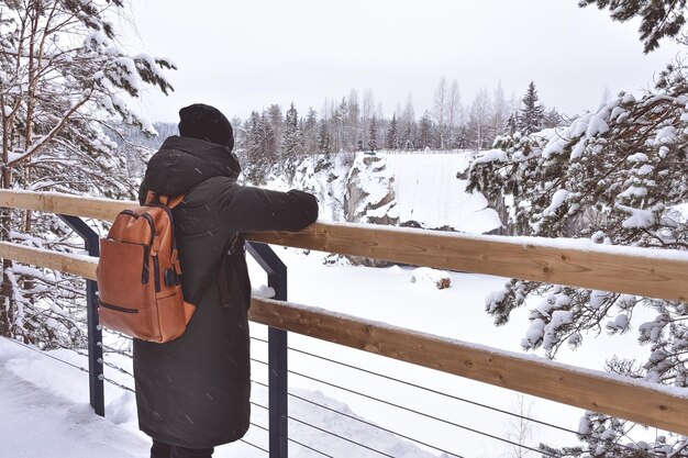 The girl stands on the bridge and looks at the winter landscape