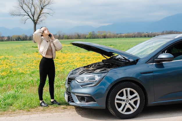 A girl stands next to a car with an open hood
