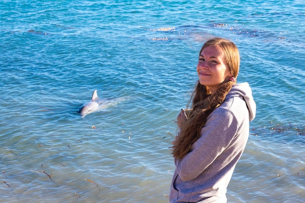 girl stands at the edge of the ocean looking at a dolphin in monkey mia, francois peron, australia