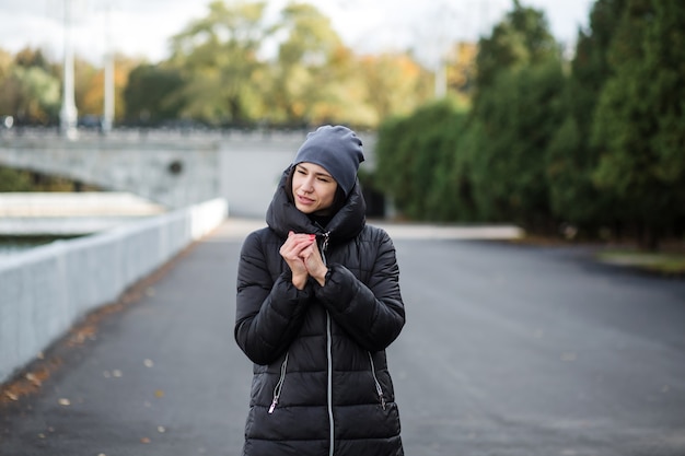 A girl stands on the embankment near the water, in warm clothes. 