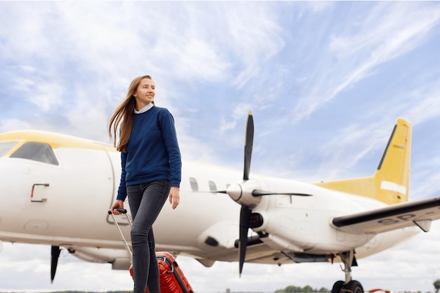 The girl stands in front of the plane with a suitcase and is going on a trip Concept for tourism