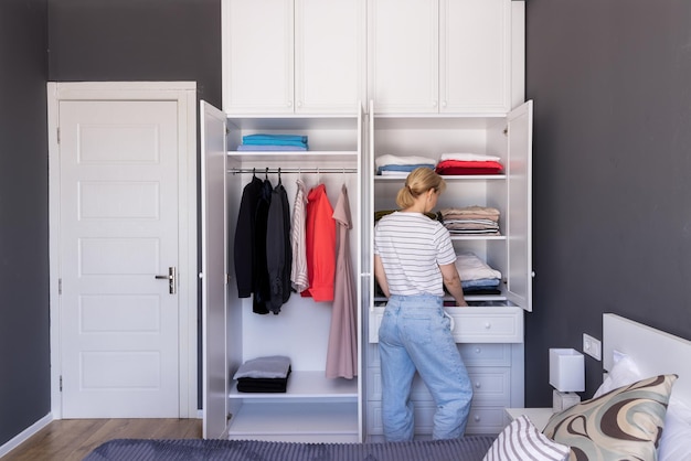 Girl stands near the closet puts things in order on the shelves with underwear