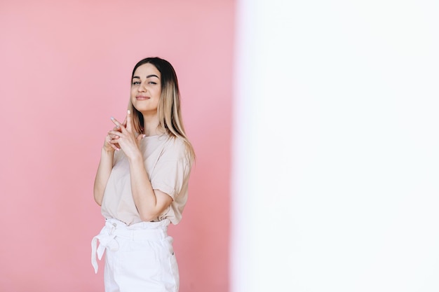 A girl stands and playfully looks at the camera on a pink background half a white background