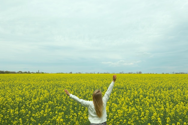 A girl stands in a rapeseed field on a summer day