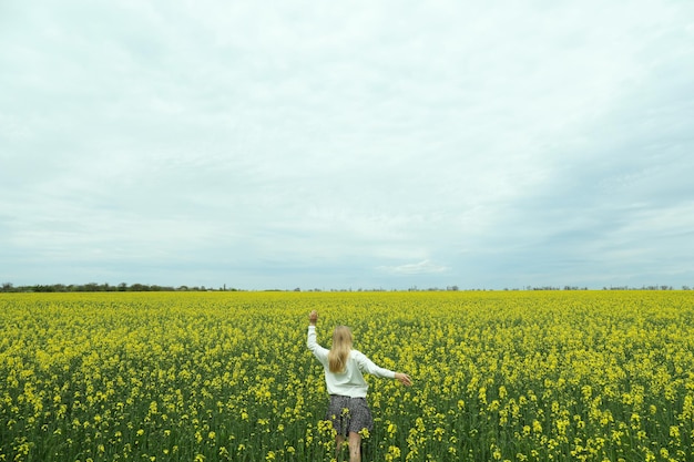 A girl stands in a rapeseed field on a summer day