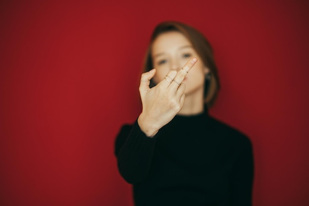 Girl stands on red background and shows middle finger in camera gesture FUCK concept Focus on girl hand with FUCK gesture Isolated background Copy space