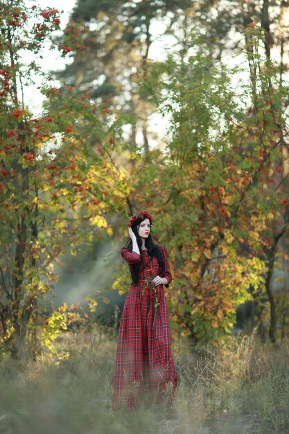 A Girl stands under a rowan in an autumn park.