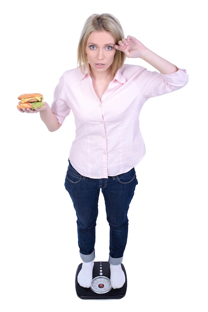 The girl stands on the scales and eat fast food.