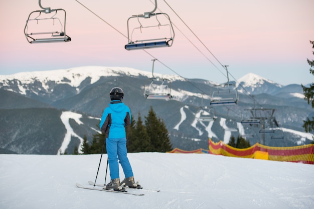 Девушка стоит на лыжах под подъемником спиной
