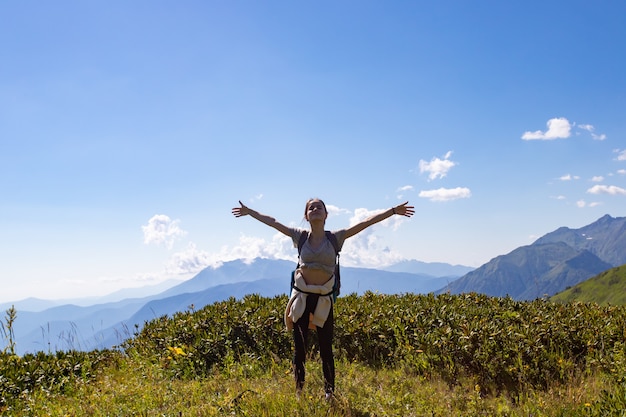 A girl stands on top of a mountain hands up