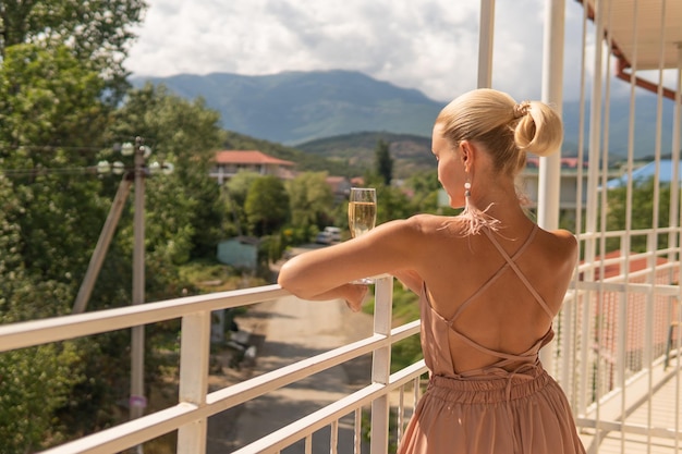 Girl stands with champagne on the mountain balcony and the blue sky against the background of