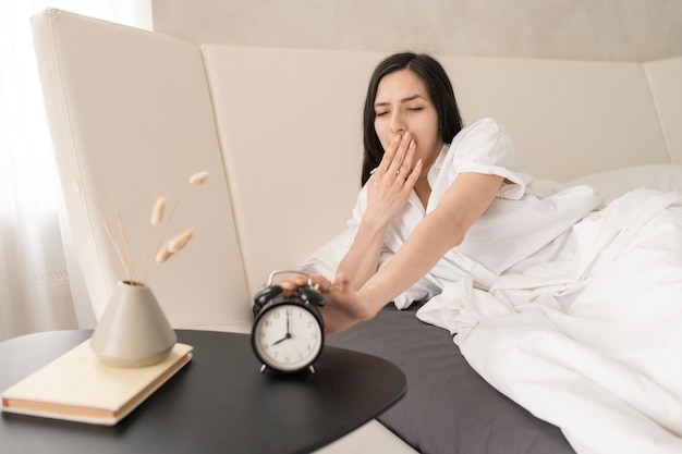 Photo girl stopping alarm clock and yawning after sleep