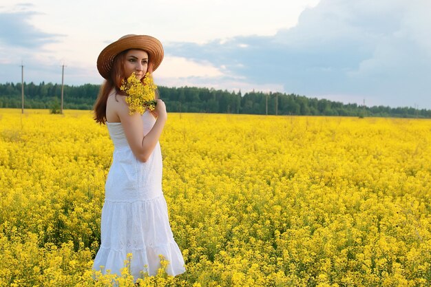 Girl in straw hat in field of yellow flowers blossoming