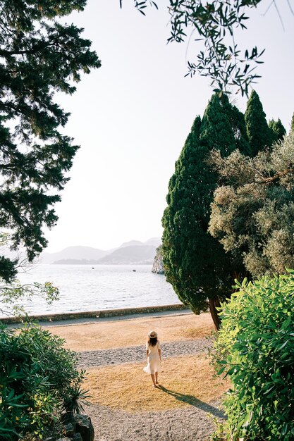 Girl in a straw hat goes to the sea from the park back view