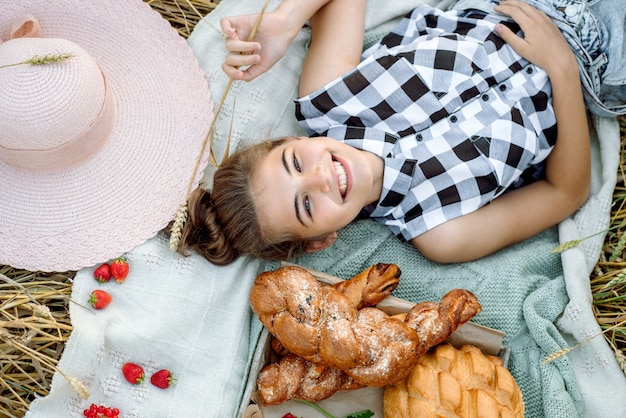 Girl in straw hat on picnic.Top view. Aesthetic picnic outdoors withbread and fruit, berries and croissants.