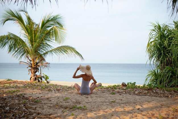 Photo girl in a straw hat sits and has a striped bathing suit on her exotic vacation beach on tropical is