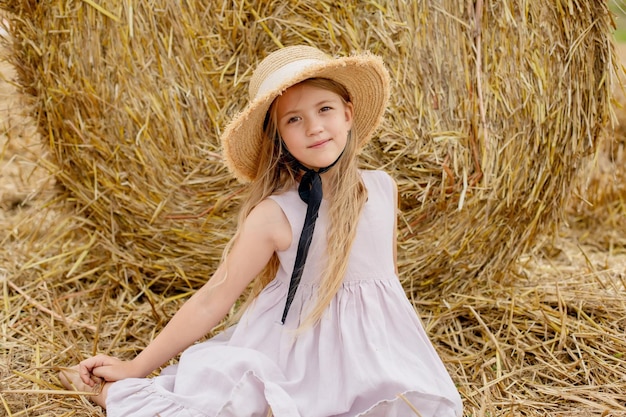 A girl in a straw hat sits in a hay field.